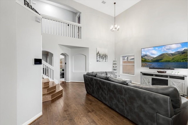 living room featuring a notable chandelier, dark wood finished floors, arched walkways, baseboards, and stairs