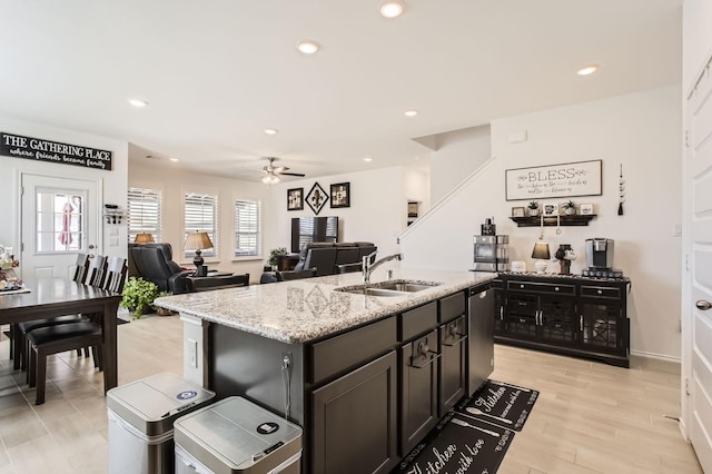 kitchen featuring a center island with sink, dishwasher, light stone counters, recessed lighting, and a sink