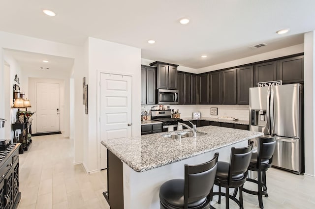 kitchen featuring visible vents, light stone counters, decorative backsplash, appliances with stainless steel finishes, and a sink