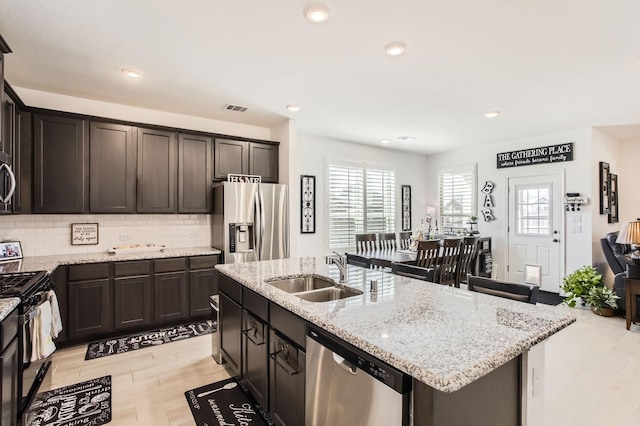 kitchen with light stone countertops, dark brown cabinetry, decorative backsplash, appliances with stainless steel finishes, and a sink