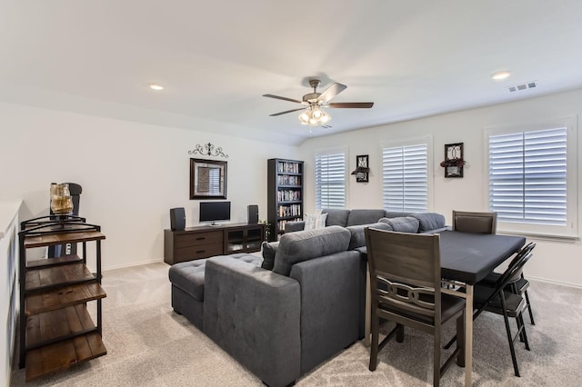 living room featuring visible vents, light colored carpet, baseboards, and a ceiling fan