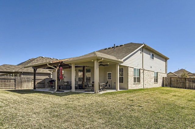 rear view of property featuring a lawn, a patio, a fenced backyard, brick siding, and ceiling fan