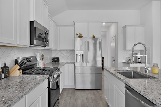 kitchen with light stone countertops, a sink, stainless steel appliances, white cabinetry, and backsplash