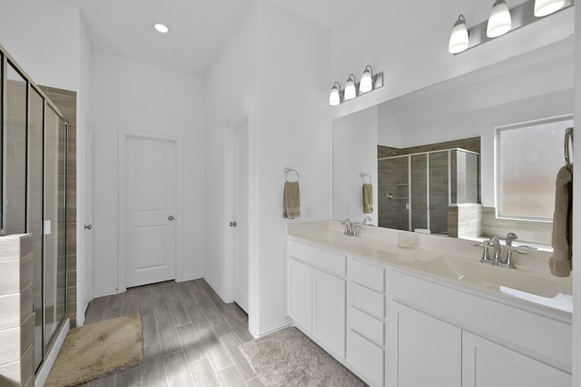 full bath featuring double vanity, wood finish floors, a stall shower, and a sink