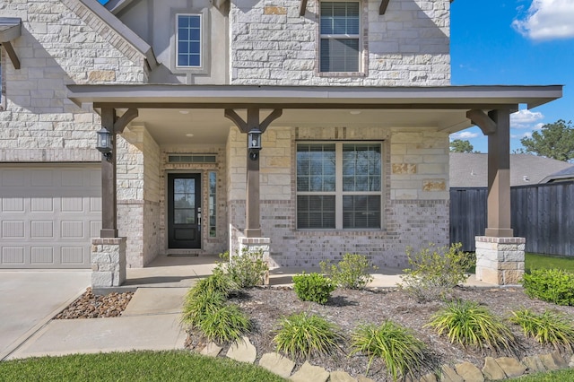 doorway to property with stone siding, a porch, an attached garage, and fence