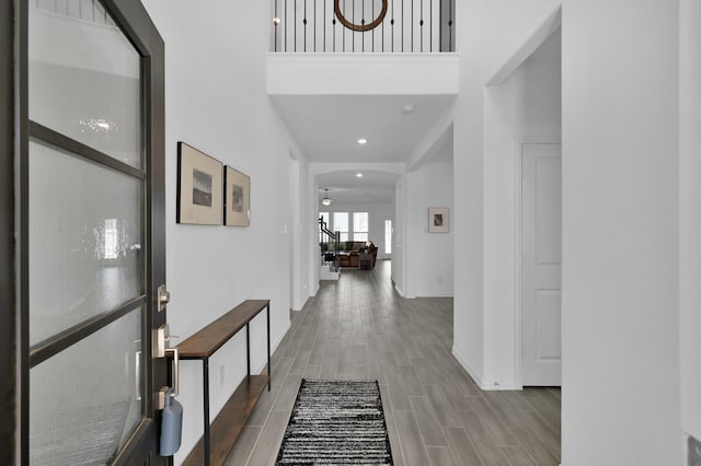 corridor featuring recessed lighting, arched walkways, a high ceiling, baseboards, and wood tiled floor