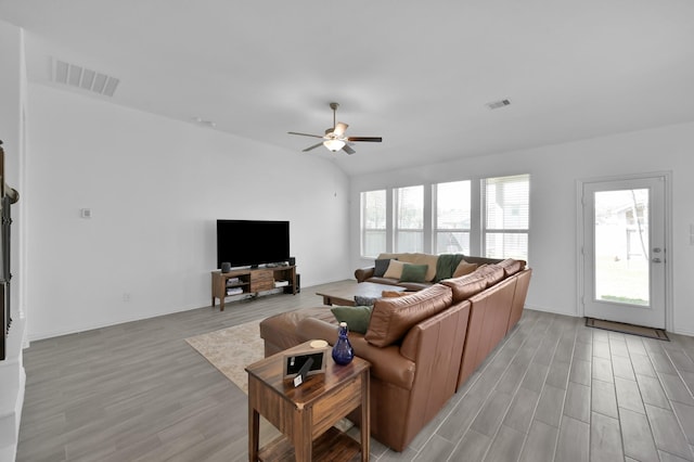 living room featuring visible vents, lofted ceiling, light wood-style flooring, and a ceiling fan