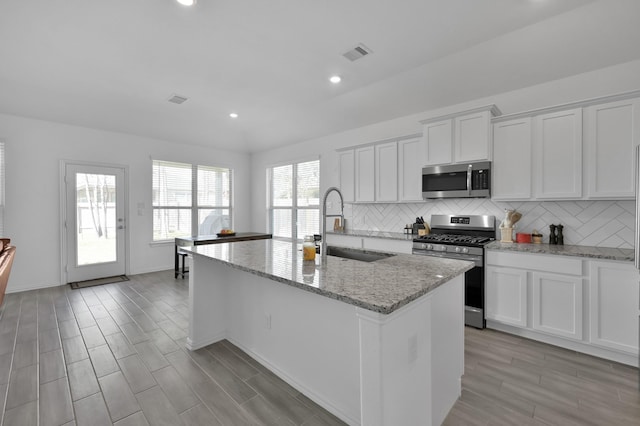 kitchen featuring visible vents, an island with sink, a sink, tasteful backsplash, and appliances with stainless steel finishes