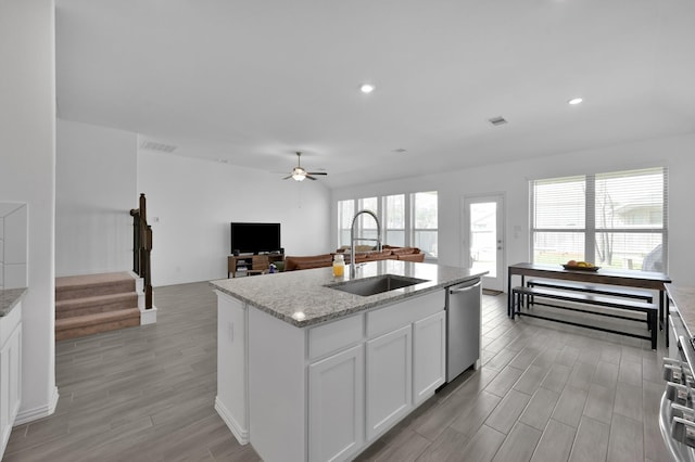 kitchen with a sink, wood finish floors, light stone counters, a ceiling fan, and stainless steel dishwasher