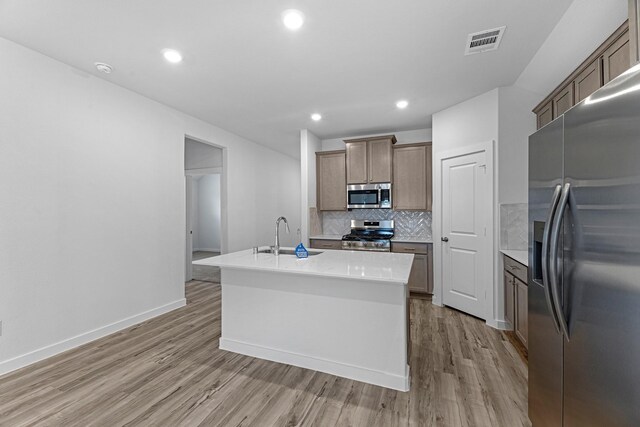 kitchen with light wood finished floors, visible vents, backsplash, stainless steel appliances, and a sink