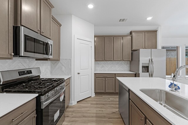 kitchen featuring a sink, stainless steel appliances, light stone countertops, and light wood-style floors