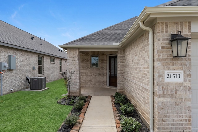 property entrance featuring brick siding, central air condition unit, a lawn, and roof with shingles