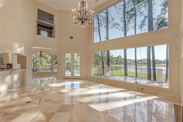 unfurnished living room with a water view, marble finish floor, ornamental molding, french doors, and a chandelier