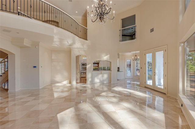 unfurnished living room with marble finish floor, french doors, arched walkways, an inviting chandelier, and baseboards