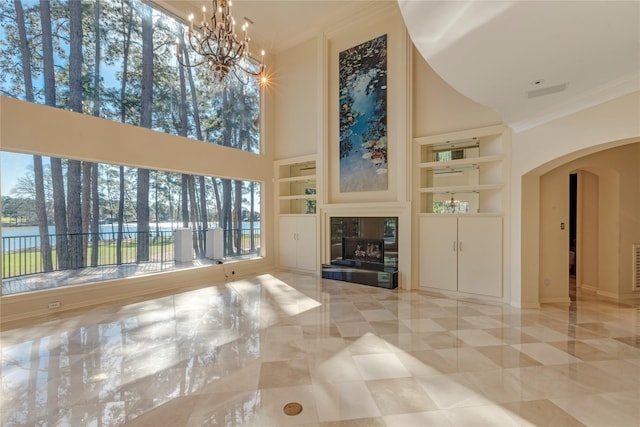 unfurnished living room featuring built in features, a high ceiling, a fireplace, arched walkways, and ornamental molding