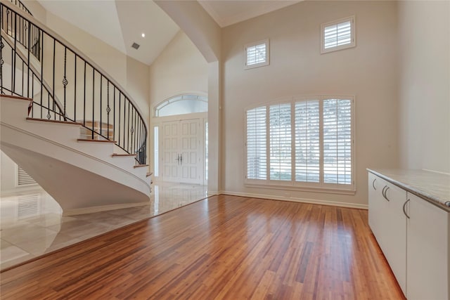 foyer entrance with baseboards, stairs, a towering ceiling, and wood finished floors