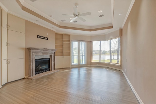 unfurnished living room featuring baseboards, visible vents, light wood-style flooring, a high end fireplace, and a raised ceiling