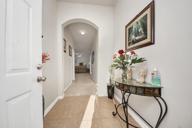 corridor featuring light tile patterned floors, baseboards, and arched walkways