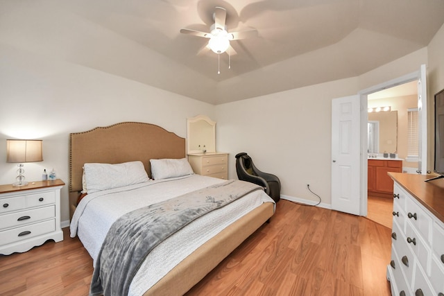 bedroom featuring a tray ceiling, baseboards, light wood-style floors, and ensuite bathroom