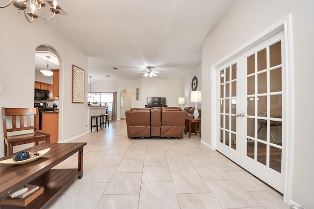 living area with baseboards, arched walkways, light tile patterned flooring, and ceiling fan with notable chandelier