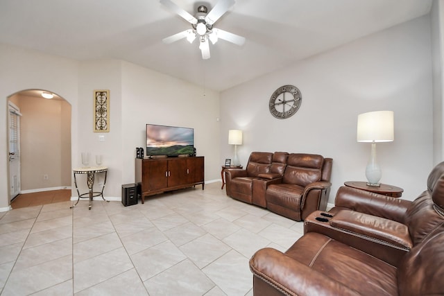 living area with light tile patterned floors, a ceiling fan, baseboards, arched walkways, and vaulted ceiling