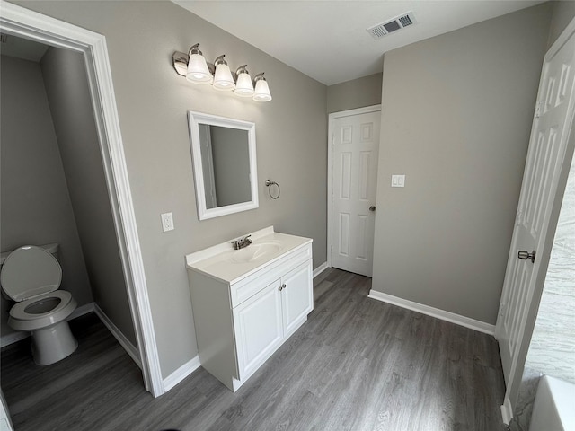 bathroom with visible vents, baseboards, toilet, wood finished floors, and vanity