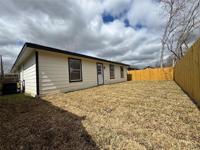 back of property with central air condition unit, a lawn, and a fenced backyard