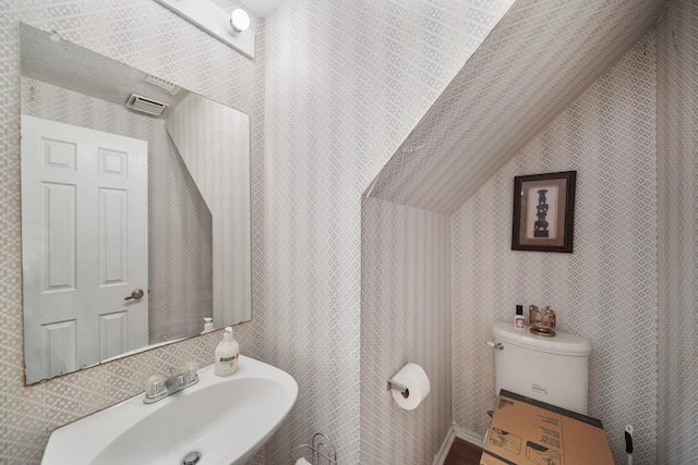 half bathroom with lofted ceiling, toilet, and a sink