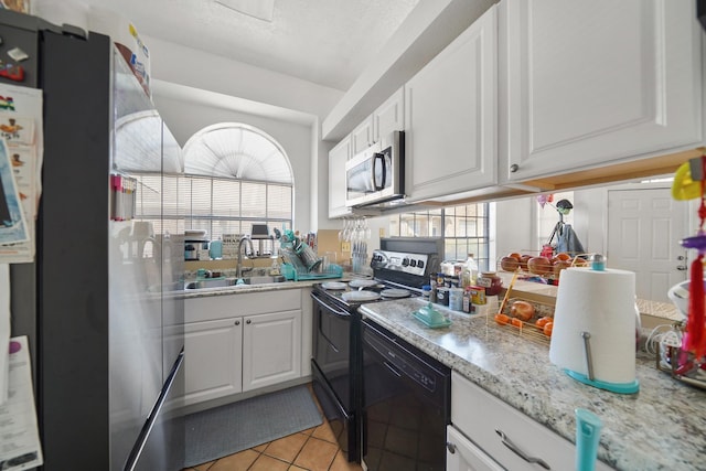 kitchen with black appliances, a sink, plenty of natural light, white cabinets, and light tile patterned flooring