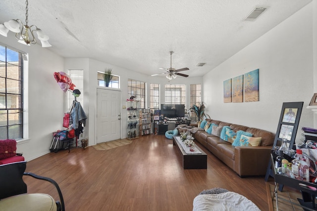 living area featuring visible vents, ceiling fan with notable chandelier, a textured ceiling, and wood finished floors