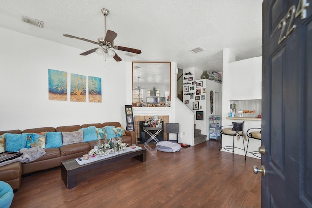 living room with a tiled fireplace, stairway, wood finished floors, a textured ceiling, and a ceiling fan