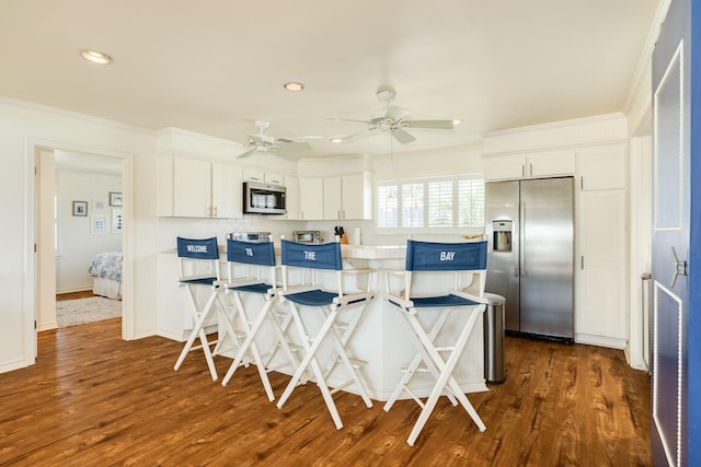 kitchen featuring backsplash, white cabinetry, stainless steel appliances, ceiling fan, and dark wood-style flooring