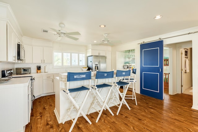 kitchen featuring a kitchen island, tile counters, dark wood-type flooring, appliances with stainless steel finishes, and a barn door