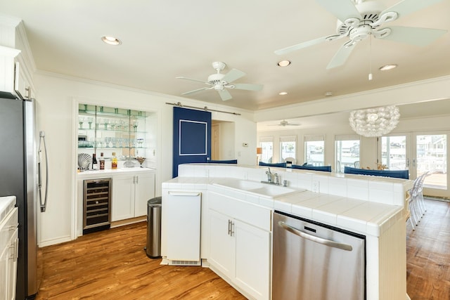 kitchen with tile countertops, beverage cooler, a sink, stainless steel appliances, and crown molding