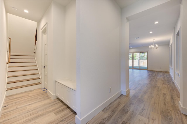 corridor featuring baseboards, a notable chandelier, and light wood-style flooring