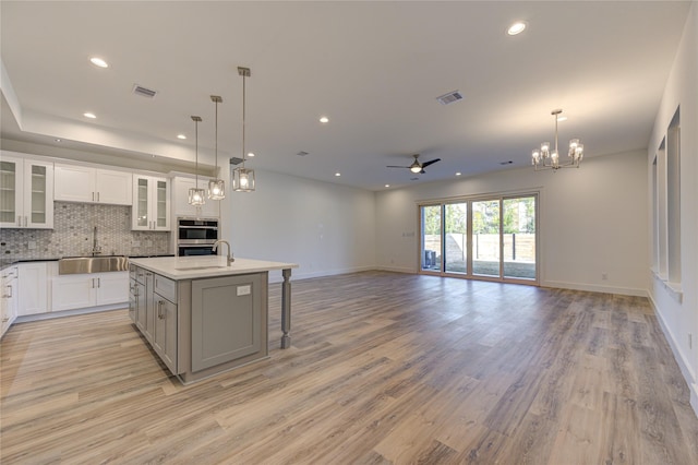 kitchen featuring tasteful backsplash, visible vents, open floor plan, an island with sink, and a sink