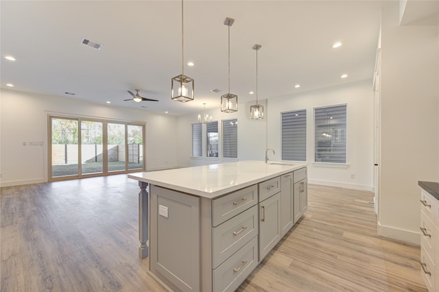 kitchen with a center island with sink, gray cabinets, a sink, light wood-style floors, and open floor plan