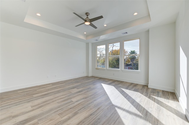 empty room featuring light wood-style floors, a raised ceiling, recessed lighting, and baseboards