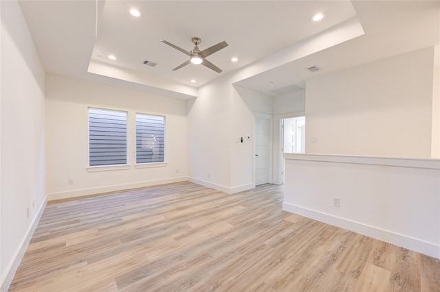 spare room featuring a ceiling fan, baseboards, light wood finished floors, recessed lighting, and a raised ceiling