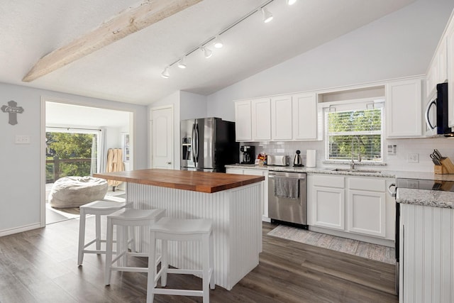 kitchen with butcher block countertops, a kitchen island, stainless steel appliances, white cabinets, and lofted ceiling