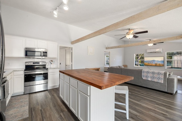 kitchen featuring wooden counters, lofted ceiling with beams, stainless steel appliances, a wall mounted air conditioner, and open floor plan