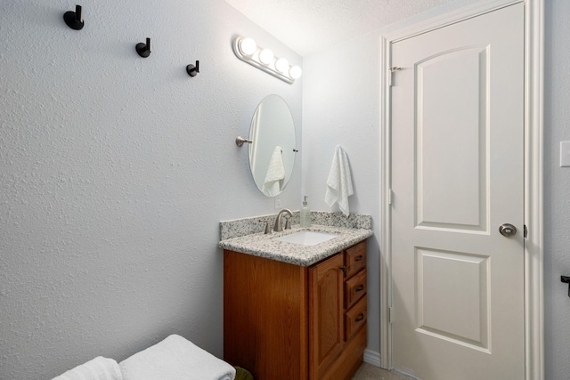 bathroom with a textured ceiling, vanity, and a textured wall