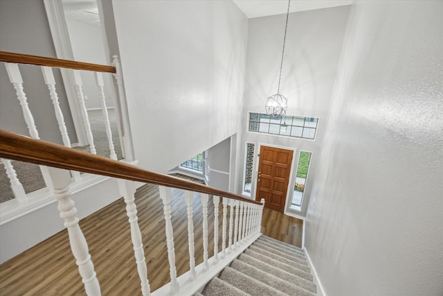 stairs featuring baseboards, a notable chandelier, a high ceiling, and wood finished floors