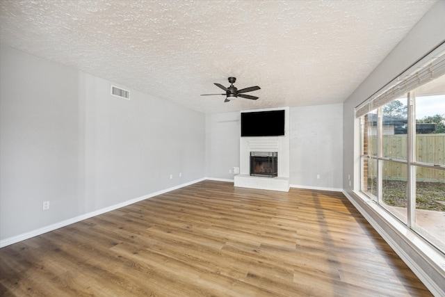 unfurnished living room featuring visible vents, a fireplace with raised hearth, a ceiling fan, a textured ceiling, and wood finished floors