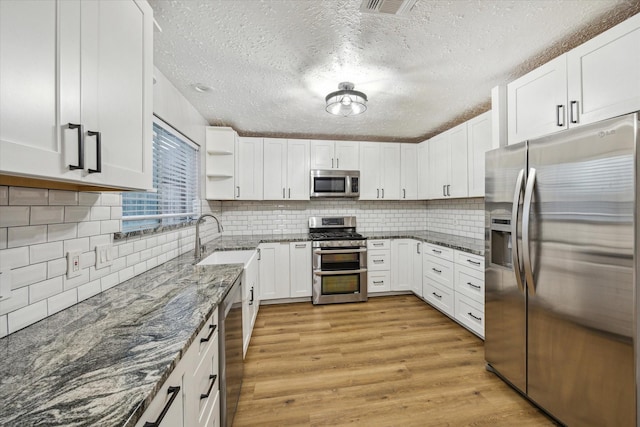 kitchen featuring backsplash, dark stone countertops, appliances with stainless steel finishes, and light wood-type flooring