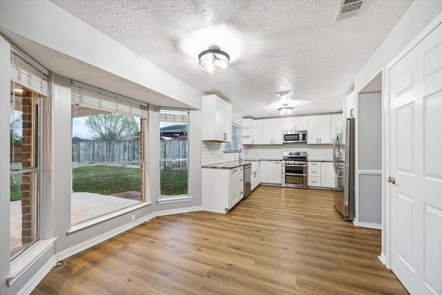 kitchen featuring wood finished floors, visible vents, stainless steel appliances, white cabinets, and backsplash