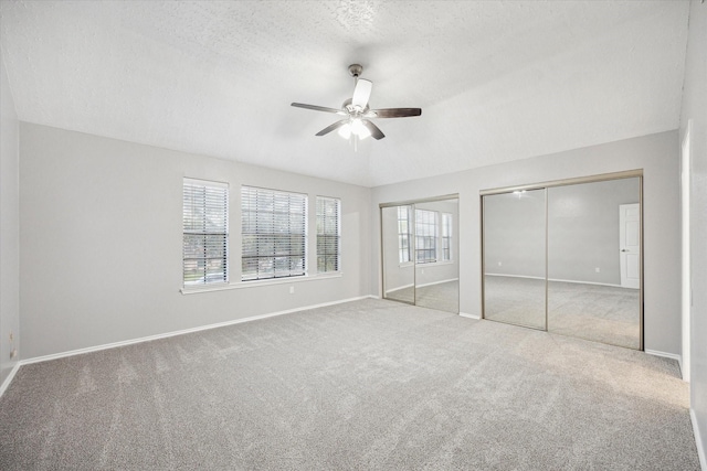 unfurnished bedroom featuring baseboards, carpet floors, two closets, and a textured ceiling