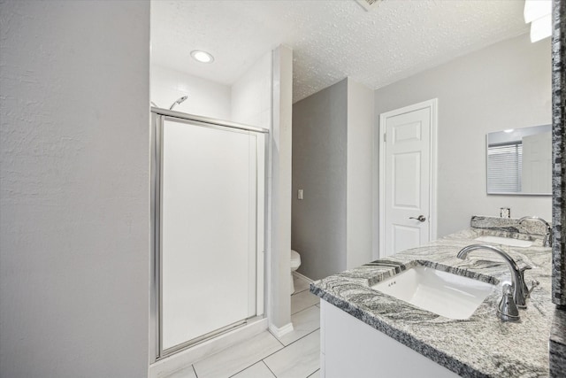 full bath featuring a sink, a textured ceiling, double vanity, and a shower stall