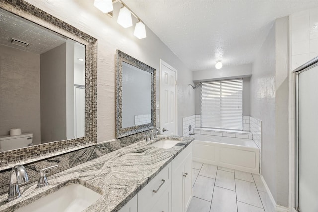 bathroom featuring visible vents, a textured ceiling, a garden tub, and a sink