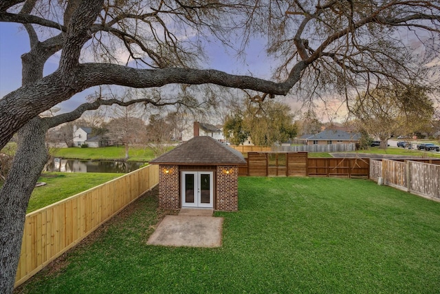 view of yard with french doors, a fenced backyard, and a water view